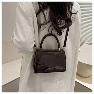 Detail einer dunkelbraunen Lackleder-Handtasche mit goldenen Beschlägen