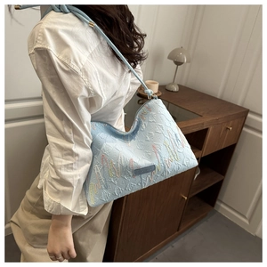Detail of light blue embroidered tote bag with wavy patterns worn on the shoulder