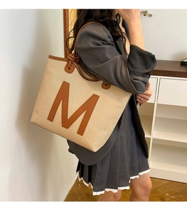 Detail of the oversized canvas tote featuring leather trim and a large letter M design
