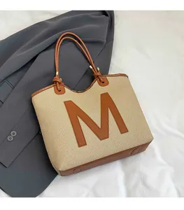 Detail of woven tote bag featuring a leather M applique and brown strap handles