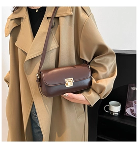 Detail einer dunkelbraunen Umhängetasche mit goldener Schnalle an einem beigen Trenchcoat