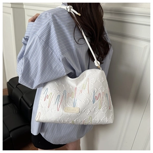 Détail du sac fourre-tout matelassé blanc avec broderie colorée et étiquette en cuir