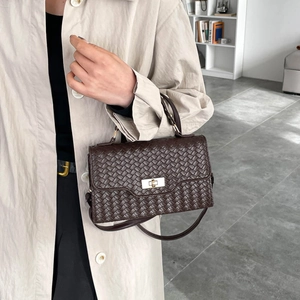 Dunkelbraune Handtasche mit Webstruktur und goldenem Drehverschluss am beigen Mantel