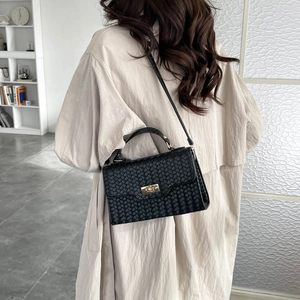 Fashion woven black crossbody handbag with gold clasp for women on bookshelf background