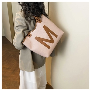 Pink woven tote bag with brown leather trim and M logo shown on model's shoulder
