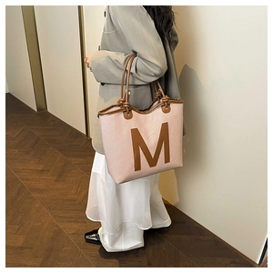 Detail of pink woven tote bag featuring brown leather M logo and rounded handles