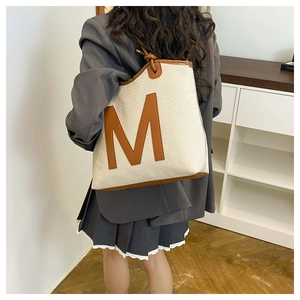 Detail of woven tote bag showing texture and leather handles on casual beige outfit