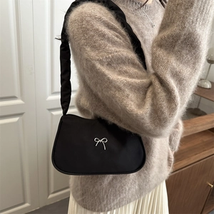 Schicke schwarze Schultertasche mit Schleife und Faltenriemen am Modell in moderner Umgebung