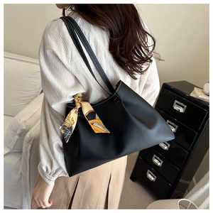Détail d'un sac à bandoulière en cuir noir avec foulard en soie jaune et surpiqûres