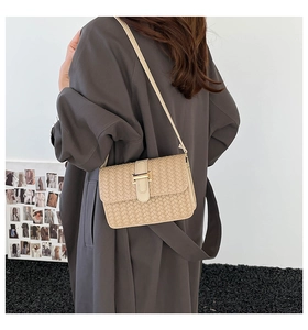 Close-up of woven texture shoulder bag with gold metal buckle on beige crossbody purse