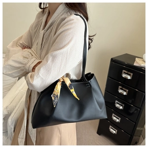 Detail of black faux leather hobo bag with decorative yellow patterned silk scarf handle