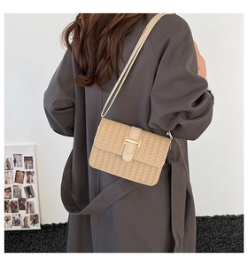 Detail of beige woven square crossbody bag with metal buckle on a shoulder strap