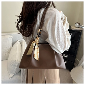 Detail of coffee brown leather tote bag featuring a decorative silk scarf on the handle