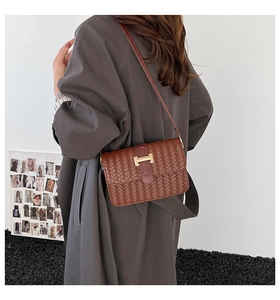 Detail of a brown woven texture shoulder bag with gold H-buckle worn by a model