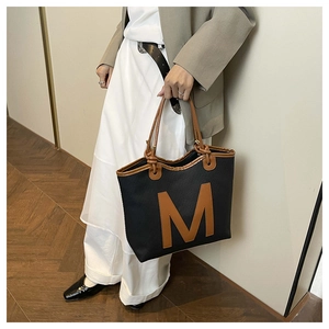 Macro view of canvas tote bag with leather trim and distinctive M letter patch detail