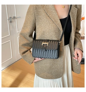 Detail of black woven leather crossbody bag with elegant gold T-clasp and strap