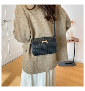 Detail of black woven crossbody bag with gold buckle on a model in a modern room