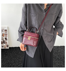 Detail of burgundy crocodile-textured box bag with golden zipper and crossbody strap