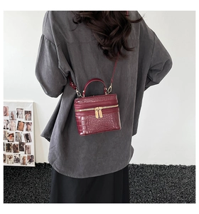 Detail shot of a dark red crocodile pattern square crossbody bag with gold zippers