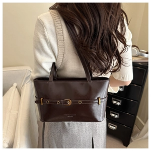 Detailed view of deep brown glossy leather tote bag with gold buckle belt and fashion text