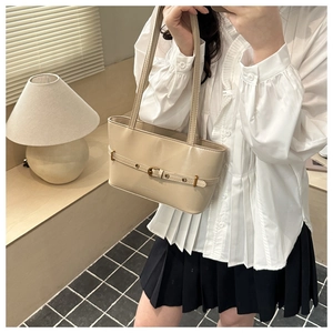 Detail of cream shoulder tote bag with buckle strap on a model in a warm interior