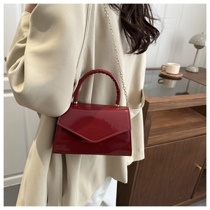 Chic red patent leather crossbody bag with gold chain strap on a stylish model