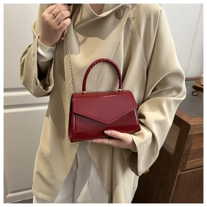 Close-up of a glossy red patent leather handbag with spiral handle and gold chain strap