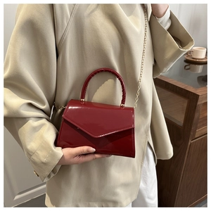 Close-up of bright red patent leather mini square bag with gold chain and woven handle