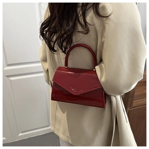Deep red patent leather crossbody bag with gold chain strap shown on a beige trench coat