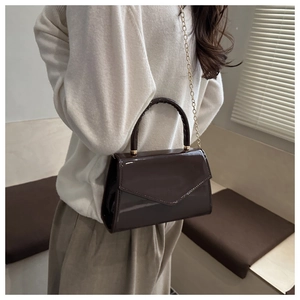 Detail of dark brown glossy patent leather crossbody bag with gold chain and top handle