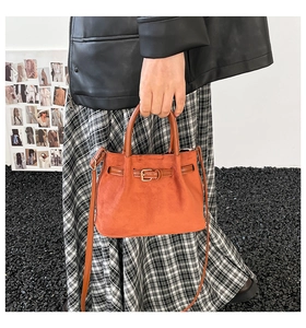 Detail of orange matte bucket bag with buckle decoration and round handle held by model