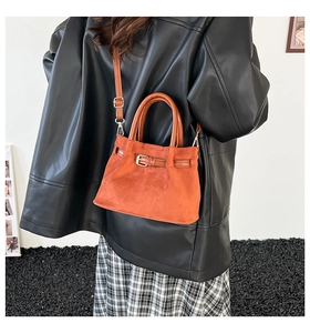 Brown suede crossbody bucket bag styled with a leather jacket in a minimalist setting