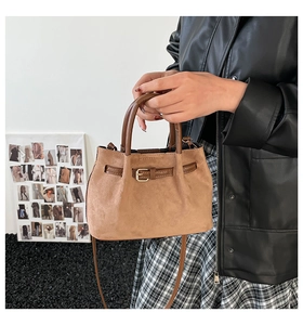 Close-up of brown suede handbag featuring decorative buckle and dual tubular handles