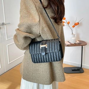Chic black woven crossbody bag with gold H clasp worn by model in a warm indoor setting
