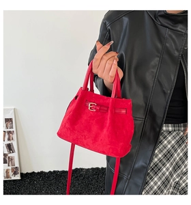 Detail of red suede crossbody bag featuring soft pleated texture and metal buckle accents