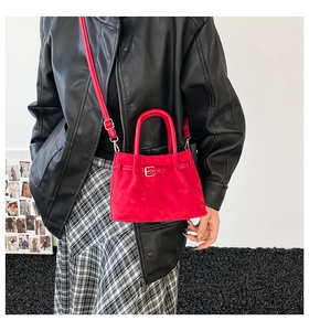 Detail of red suede mini bucket bag featuring decorative buckle and adjustable strap
