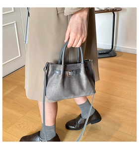 Detailed side view of dark grey suede handbag with gold buckle and adjustable strap