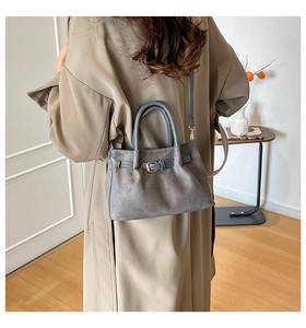 Gray suede bucket bag with blue straps styled on a trench coat for an elegant look