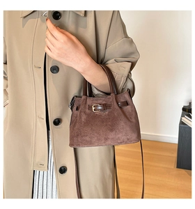 Detail of dark brown suede handbag with metallic eyelet strap and leather handles