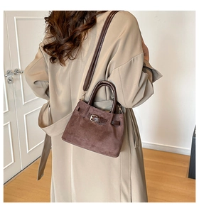 Deep brown suede bucket bag with gold hardware worn as a crossbody with a beige coat
