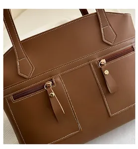 Detail of brown leather tote bag with white stitching and gold zipper rivets