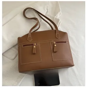 Macro view of brown faux leather shoulder bag with white stitching and twin front zip pockets