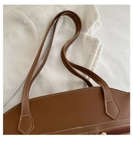 Detail of a brown leather tote bag showing white contrast stitching and zip closure
