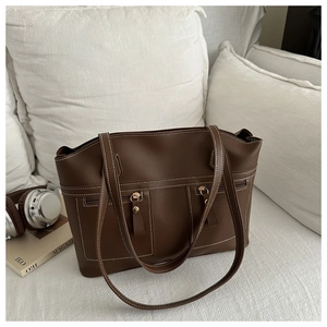 Close-up of large dark brown tote bag with white stitching and front zipper pockets