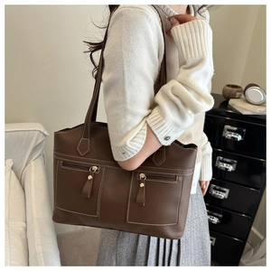 Detail of dark brown tote bag featuring white contrast stitching and dual front zip pockets