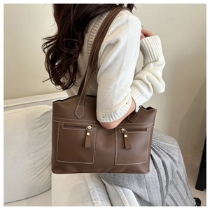 Detail of dark brown leather tote bag with white stitching and front zipper pockets