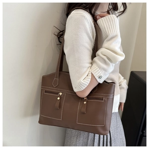 Close-up of brown matte leather tote bag featuring white stitching and dual front pockets