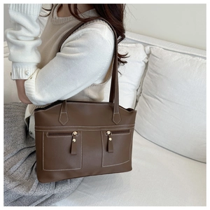 Detail of dark brown faux leather tote bag with white contrast stitching and zip pockets