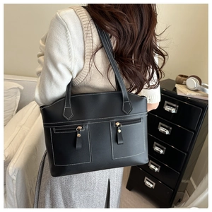 Detail of large black leather tote bag featuring white stitching and gold zip hardware
