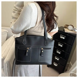 Detail showing black tote bag with white contrast stitching and gold ring zippers